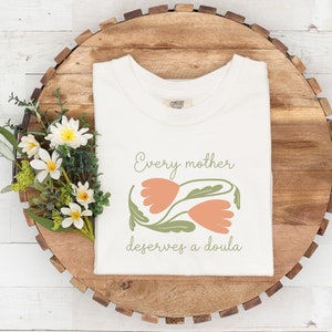 White T-shirt with 'Every mother deserves a doula' print and hands-leaf graphic