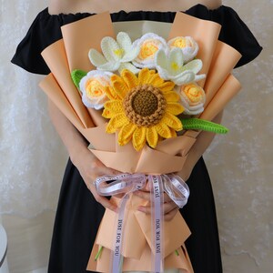 Crochet flower bouquet with yellow sunflower center and white blooms, tied with blue ribbon