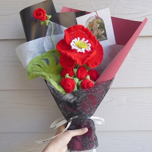 Handmade crochet flower bouquet with red blooms and green leaves, wrapped in gift paper.