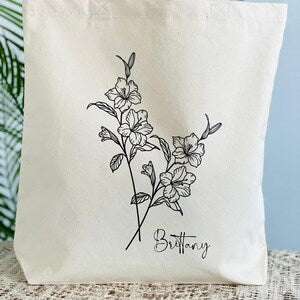 Cream canvas tote bag with black month-flower line art and cursive name Brittany