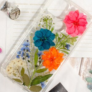 Clear pressed-flower phone case with blue, orange, and pink dried blooms