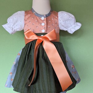 Baby dirndl dress with brown bodice, white puff sleeves, orange sash, dark green skirt