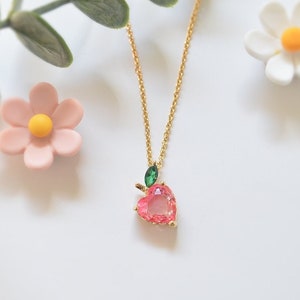 Gold chain necklace with pink heart-shaped stone pendant and small green accents