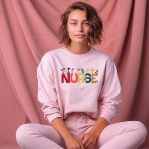 Light pink sweatshirt with colorful flower nurse emblem on chest, crewneck style