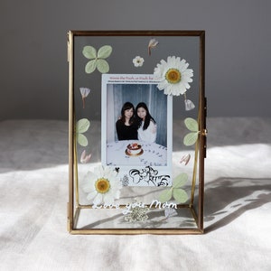 Rectangular photo frame with instant photo, pressed daisies and green leaves inside