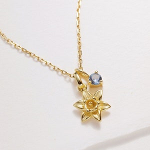 Gold-tone birth flower necklace with daffodil charm and small blue gemstone pendant