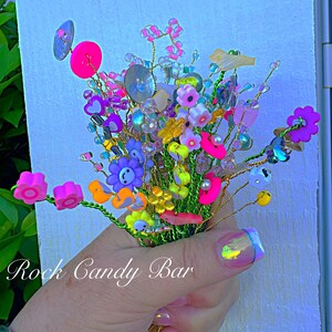 Tiny beaded flower bouquet with bright pink, blue, and yellow blooms and green leaves