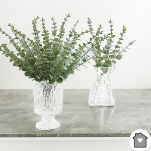 Artificial eucalyptus stems with green leaves, arranged in white vases