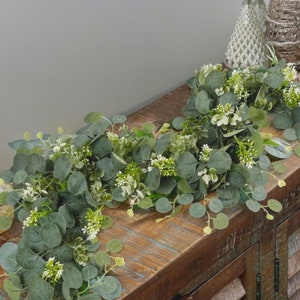 Faux eucalyptus garland with green leaves and small pale flowers, decorative greenery