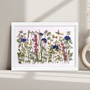 Framed pressed flower wall art with blue cornflowers, pink heathers, and yellow blossoms