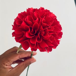 Small red paper flower with layered petals and green stem, handmade craft look
