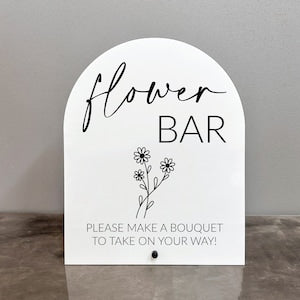 White acrylic arch sign reading 'flower' and 'BAR' with floral line art and bouquet message