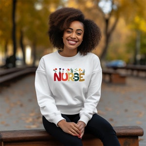 White nurse sweatshirt with red “Nurse” lettering and flower graphic on front