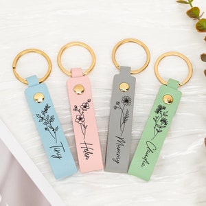 Assorted leather birth-flower keychains with engraved line-art designs and metal rings