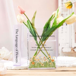 Clear acrylic book-shaped vase with printed cover and spine, holding tulip flowers