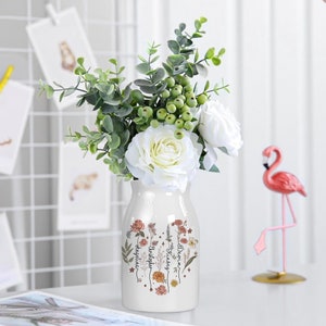 White ceramic flower vase with garden floral print holding mixed faux greenery and white roses