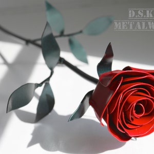 Red metal rose with spiral petals and attached green leaves on a stem