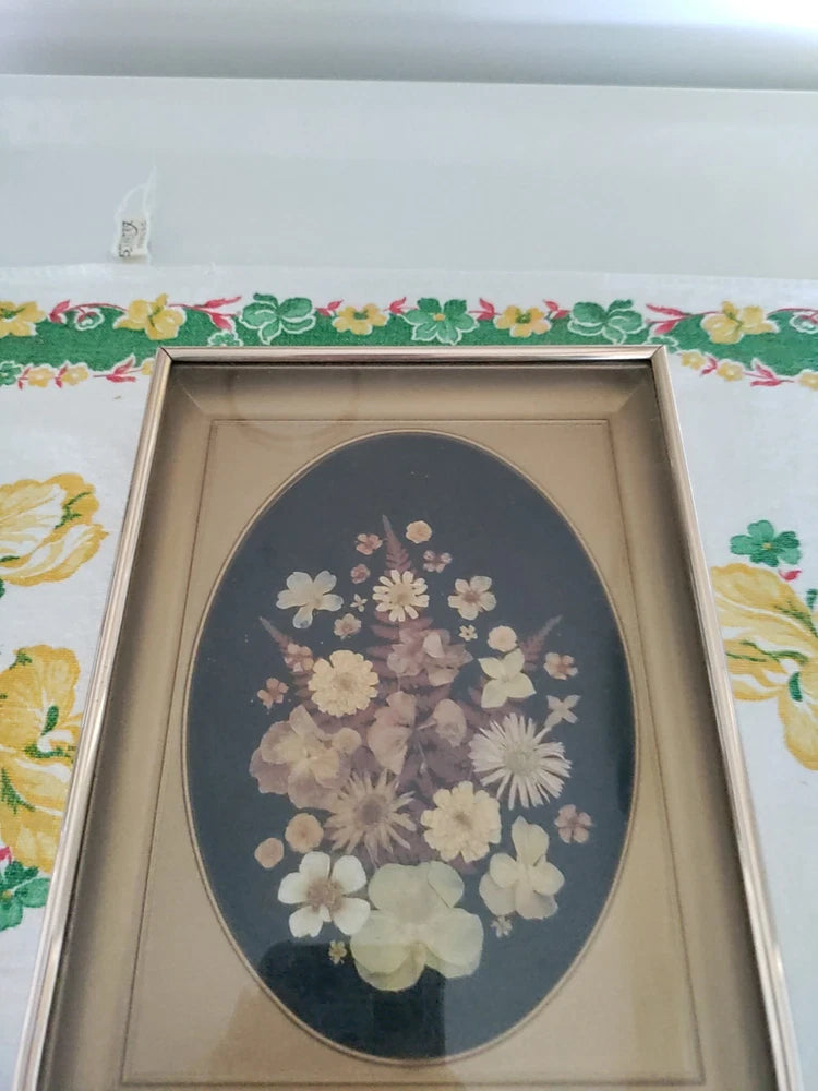 Dried flower shadow box with oval arrangement of pale blooms in a dark backing