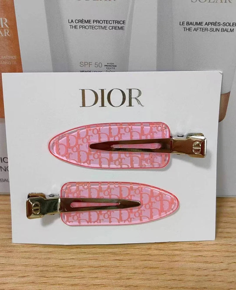 Pink hair clips with clear plastic base, gold metal hinges, on Dior card