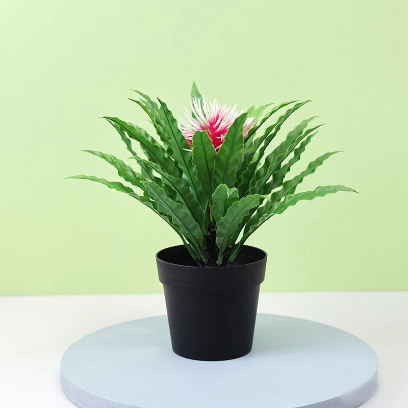 Artificial potted green plant in black pot with feathery leaves and pink bloom
