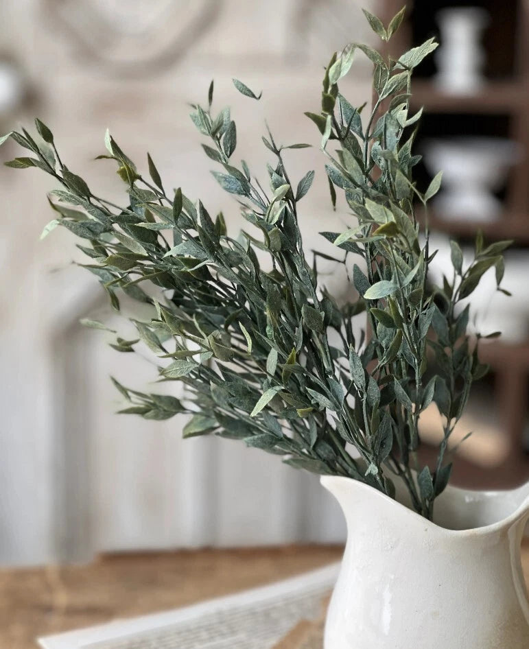 Artificial greenery stems with mixed dark green leaves, in a white ceramic vase