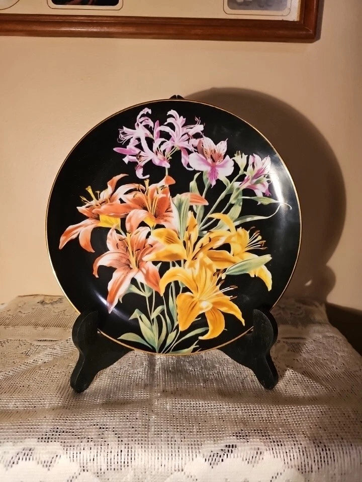 Collector plate with black background, colorful lilies bouquet, and gold rim on a stand