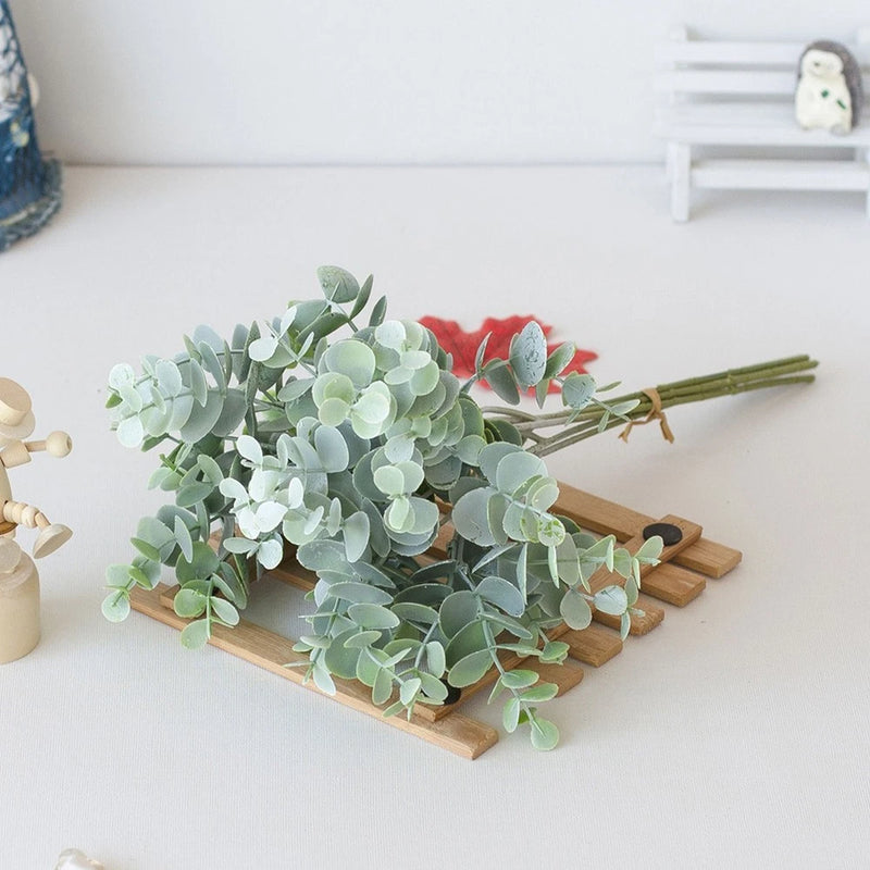 Artificial eucalyptus-style plant bouquet with pale green leaves in wooden tray