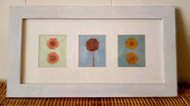 Framed dried pressed flower artwork with three square panels, floral stems and blooms.