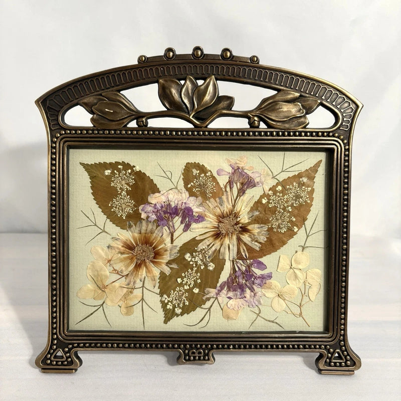 Rustic vintage pressed flower art in ornate bronze frame with purple and cream blooms