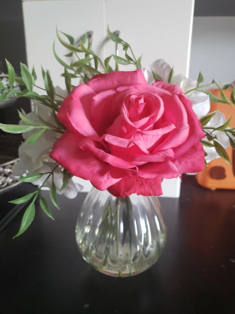 Pink artificial peony flower with green leaves in clear ribbed glass vase