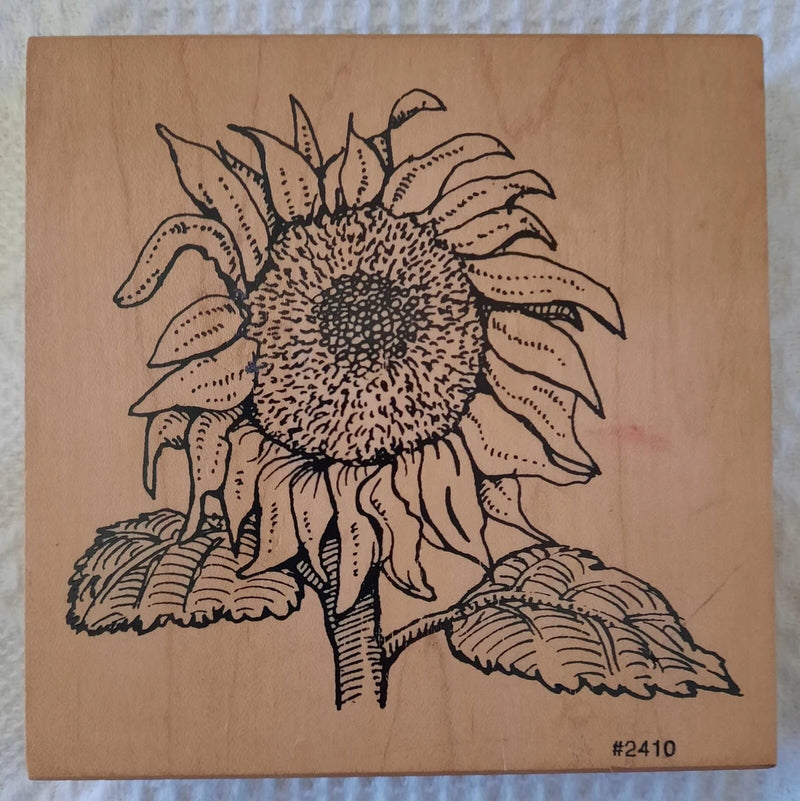 Sunflower rubber stamp with outlined blossom, leaves, and stem detail on craft backing