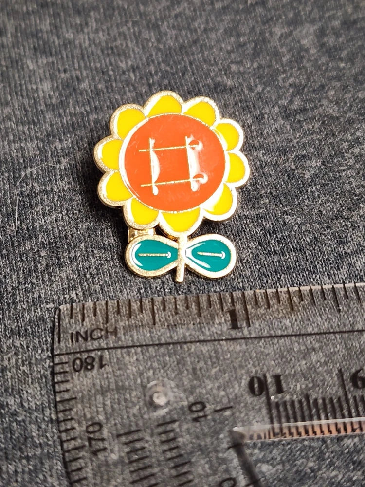 Cartoon sunflower enamel lapel pin with orange center and yellow petals, green leaves