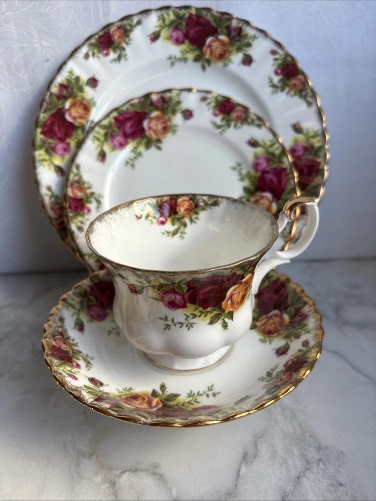 Vintage rose-pattern tea cup and saucer with gold trim, matching plates partially visible