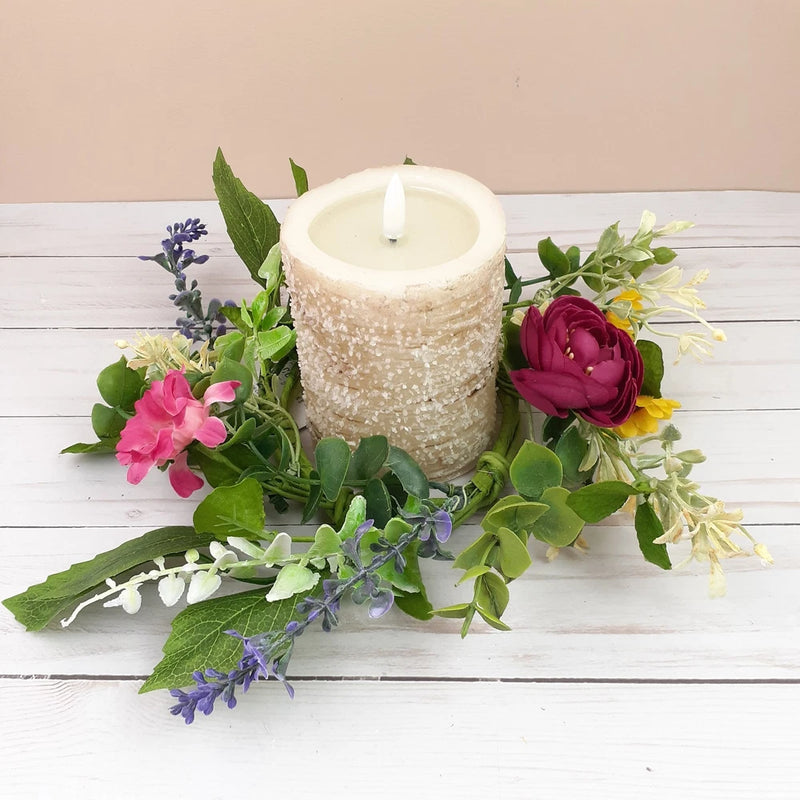 Floral candle wreath with pink and burgundy flowers, green leaves, and a white pillar candle