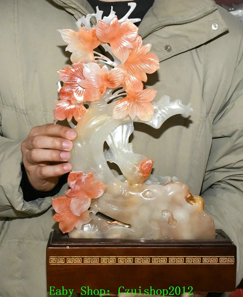 Translucent jade peony and bird carving statue on dark wooden base, pink blossoms
