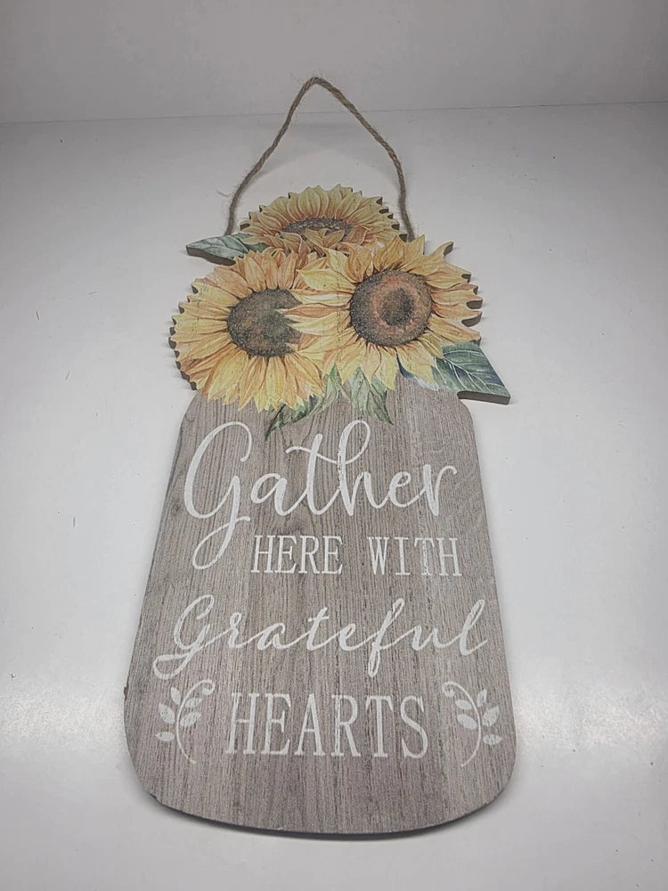 Wooden hanging sign with sunflowers and text “Gather Here With Grateful Hearts”
