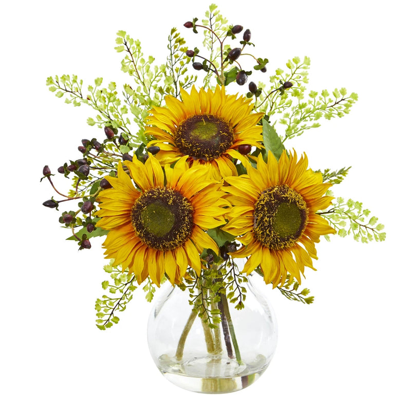 Artificial sunflower flower arrangement in clear glass vase with yellow blooms and green foliage