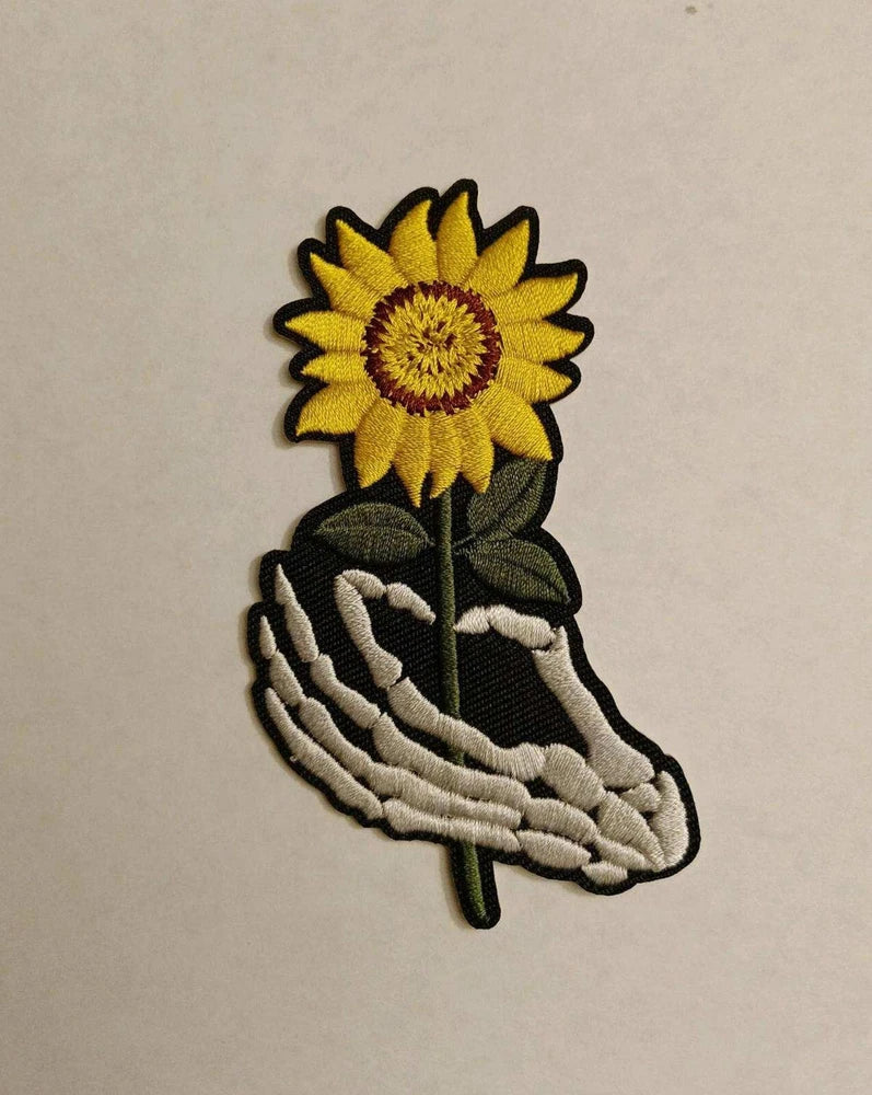 Embroidered patch: skeleton hand holding sunflower, yellow flower on dark fabric
