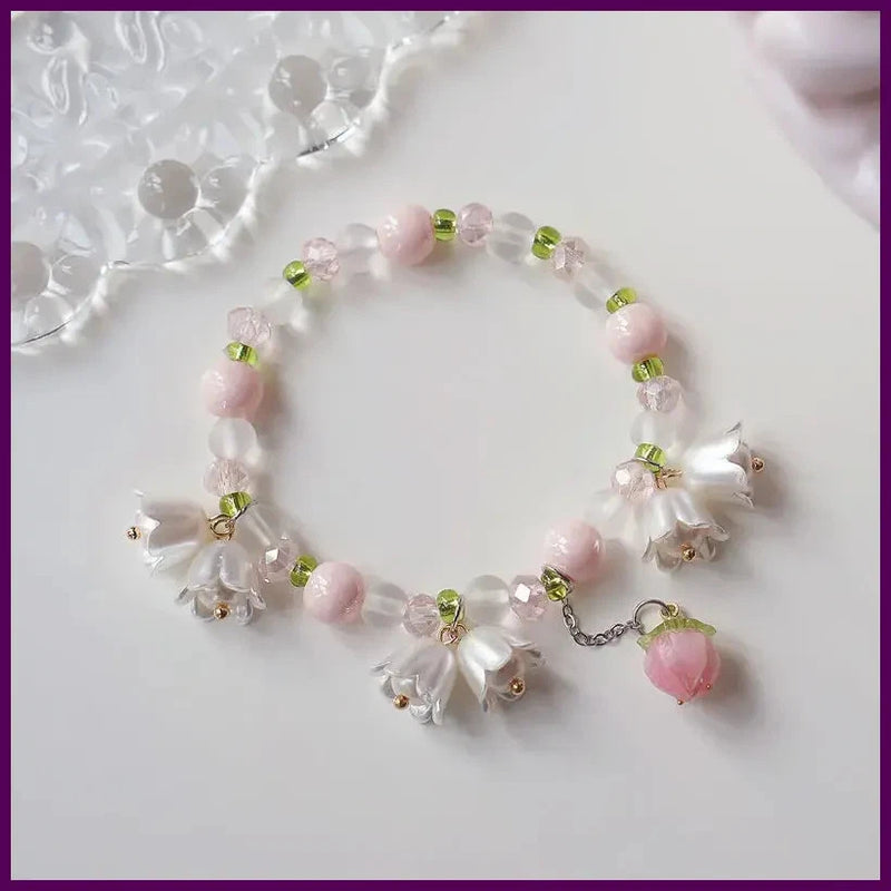 Pink lily flower bracelet with clear beads, green accents, and dangling heart charm