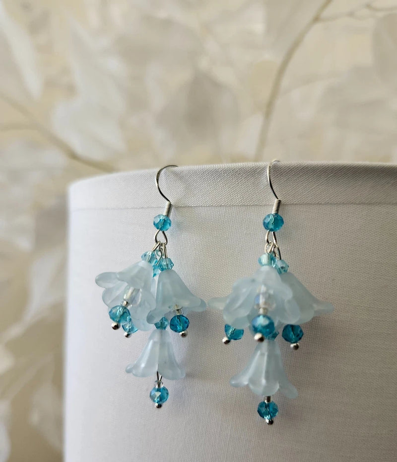 Dangling lily flower earrings with blue lucite petals, teal crystals, and silver hooks