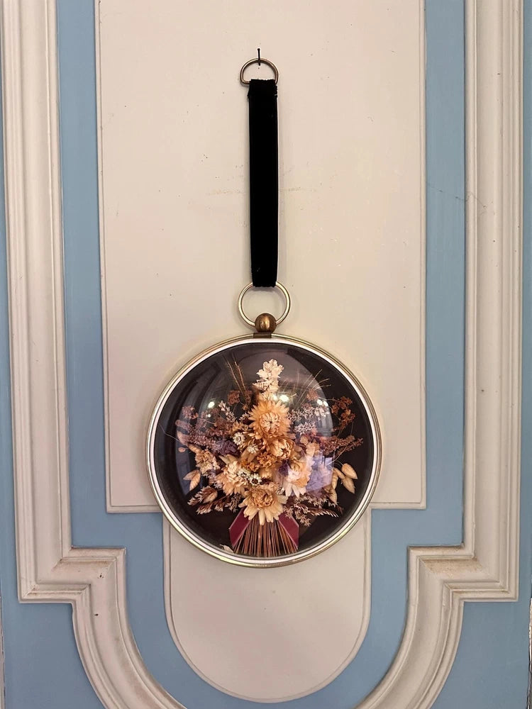 Circular glass dome dried flower wall art with hanging black strap and bouquet inside