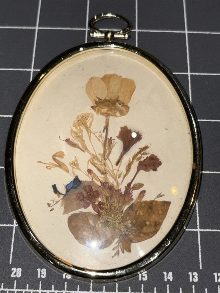 Oval hanging frame with pressed wildflowers under glass, gold-tone edge