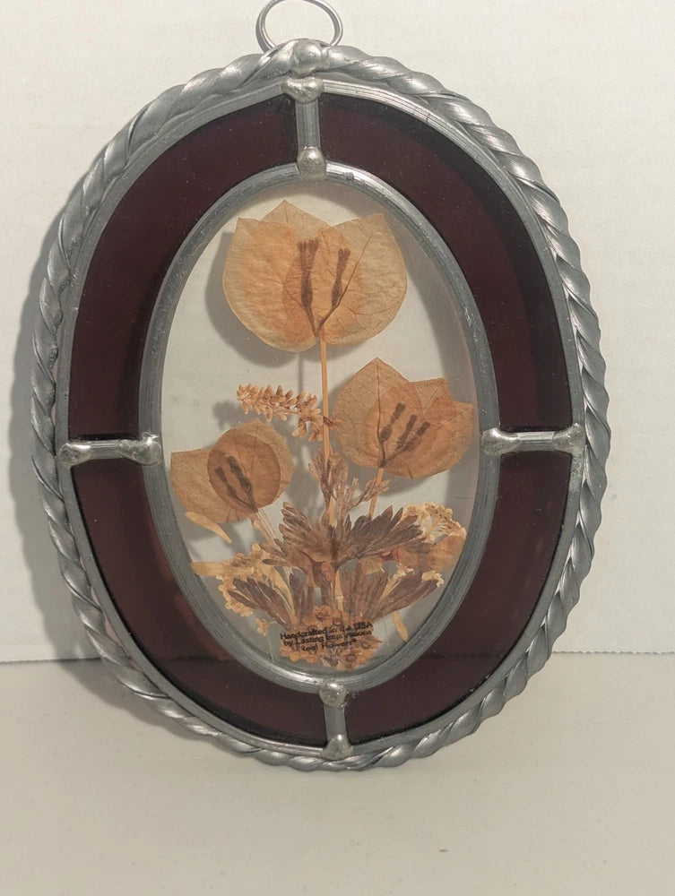 Oval glass wall hanging with pressed dried flowers in a pewter-toned frame