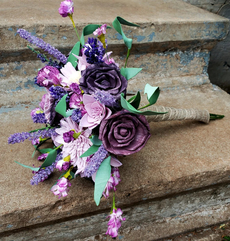 Lavender wildflower bridal bouquet with purple roses, green leaves, and twine-wrapped handle
