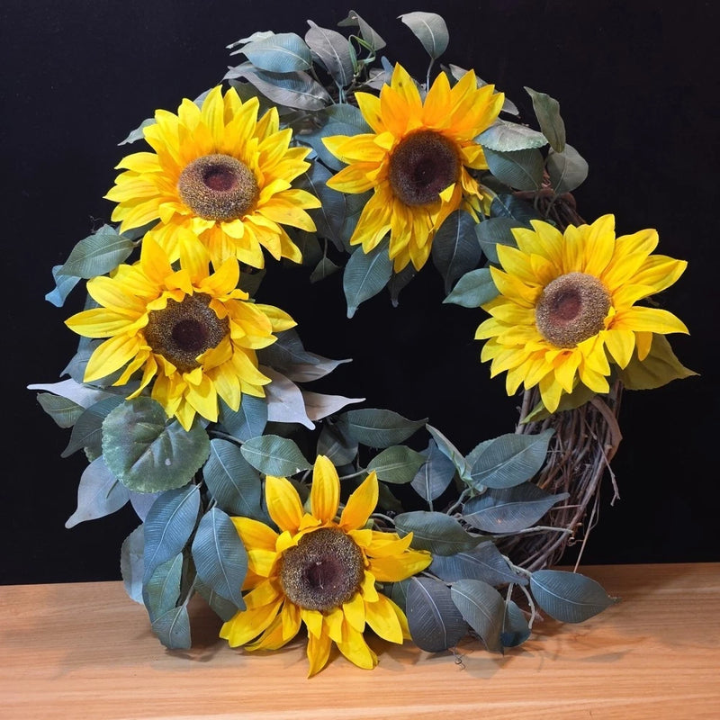 Artificial sunflower wreath with round yellow blooms and dark centers, faux green leaves.