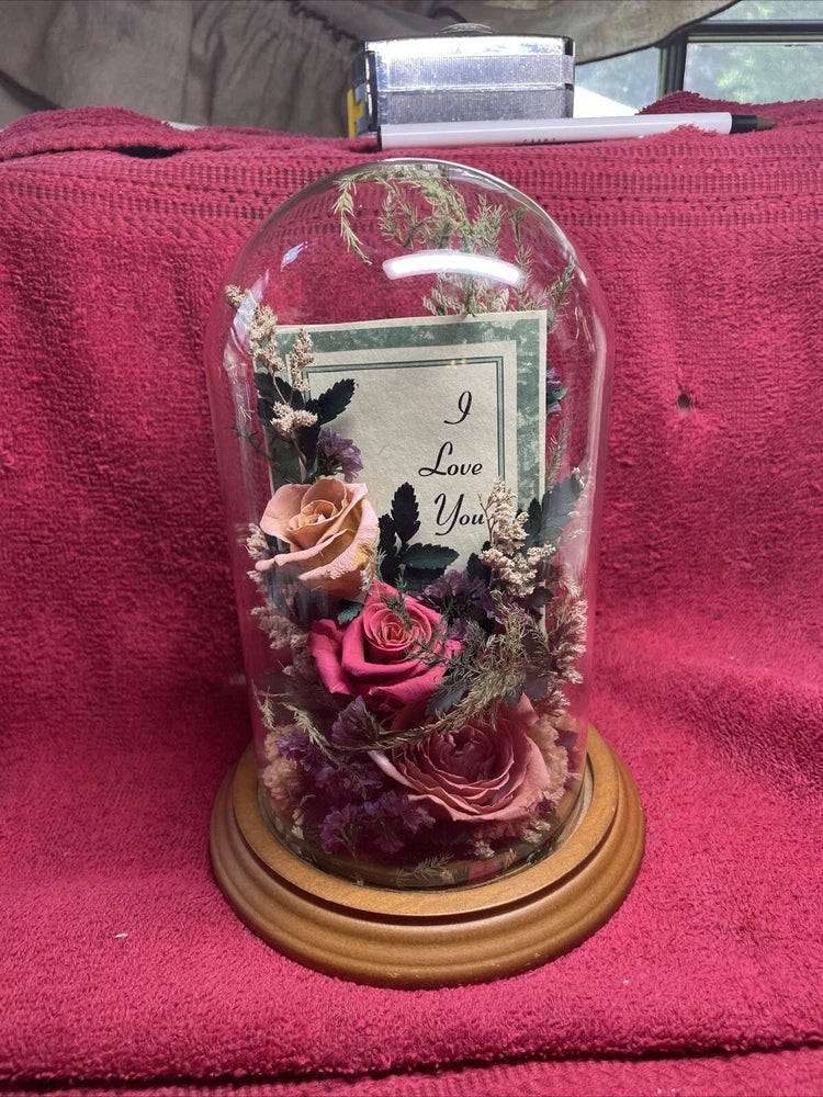 Preserved dried rose flower arrangement under clear glass dome on wooden base