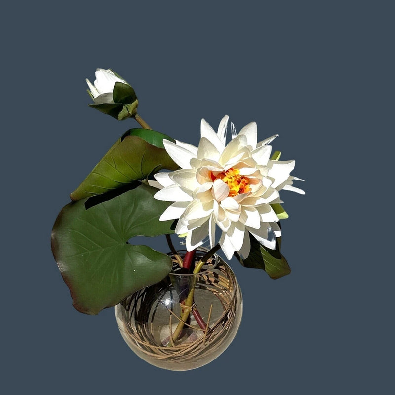 Artificial water lily floral arrangement with white bloom, green leaves, clear glass base