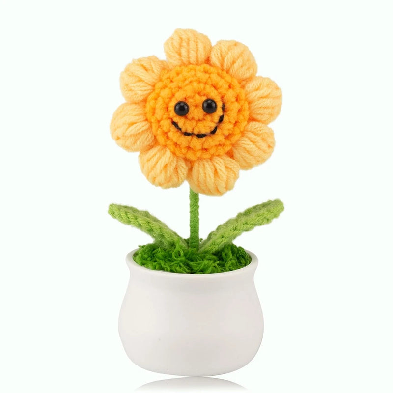Knitted orange sunflower with smiling face in white pot with green leaves