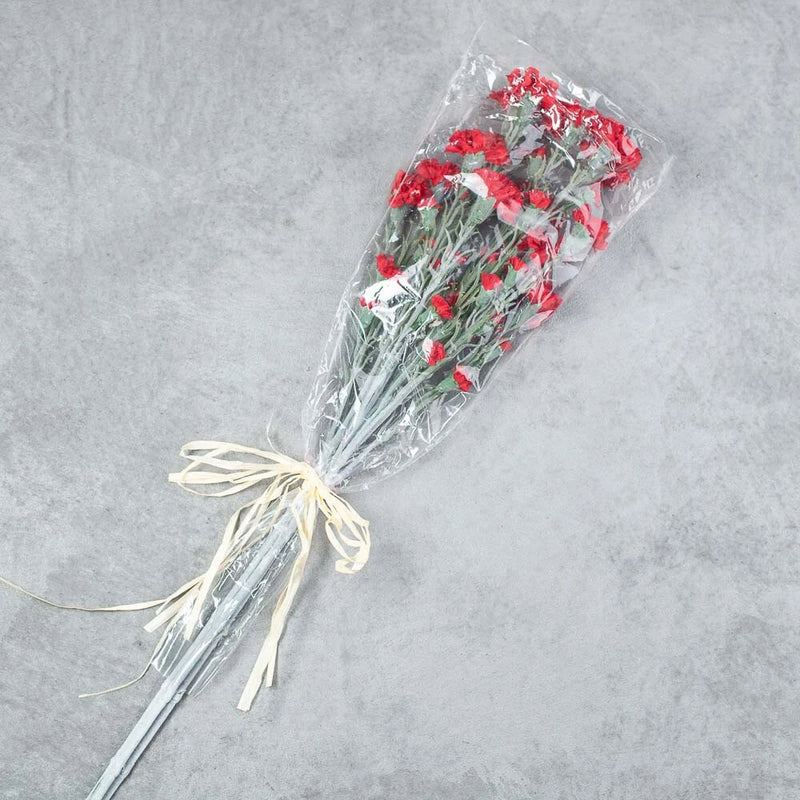 Artificial red carnation floral bundle with green leaves, wrapped and tied with ribbon
