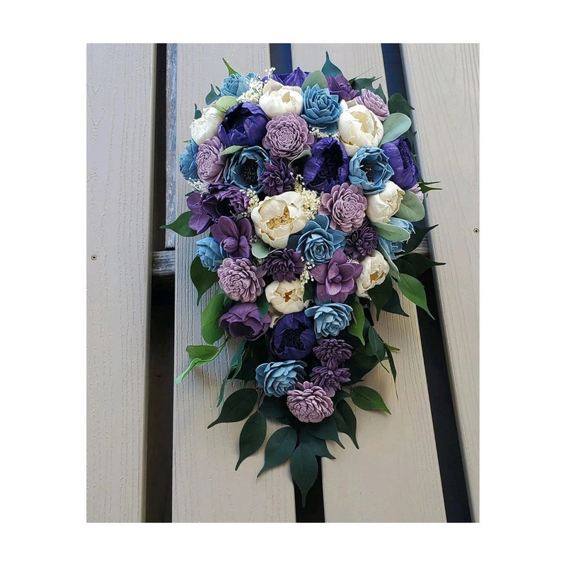 Cascade bridal bouquet of purple and blue artificial flowers with white accents and green leaves